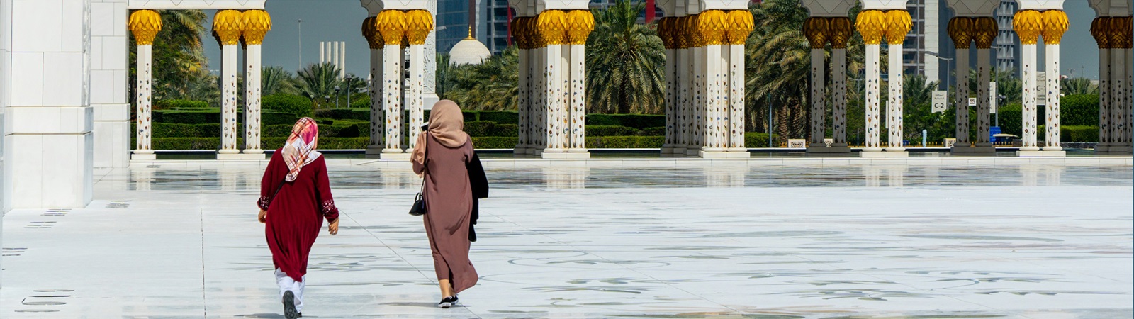 two people walking in front of a large white building with Sheikh Zayed Mosque in the background