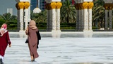 two people walking in front of a large white building with Sheikh Zayed Mosque in the background